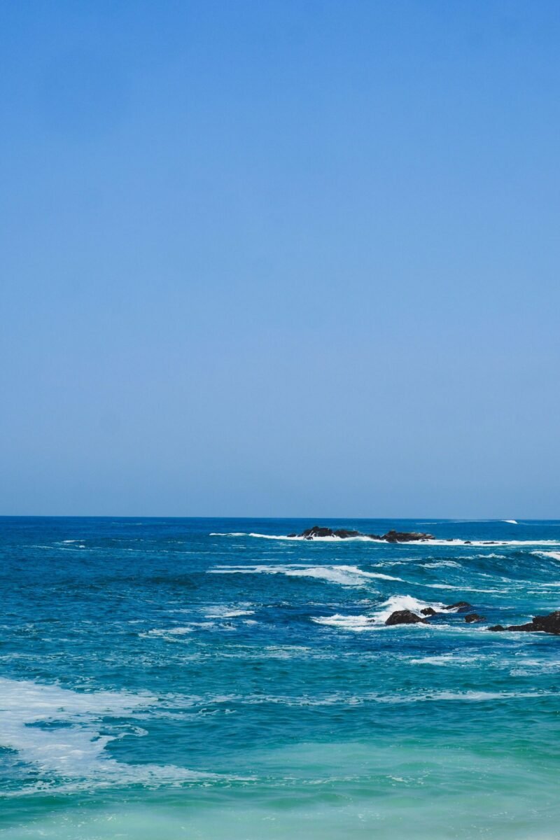 Peaceful ocean scene with waves and rocks under a clear blue sky, ideal for tranquil backdrops.