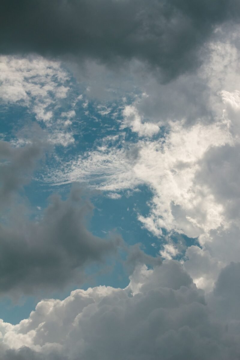 A dynamic cloudscape featuring a mix of cumulus and dark storm clouds against a blue sky.