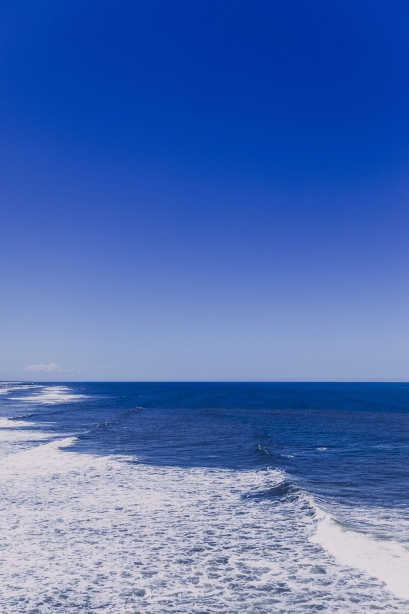 Picturesque scenery of endless blue ocean with foamy waves crashing on coast with blue sky